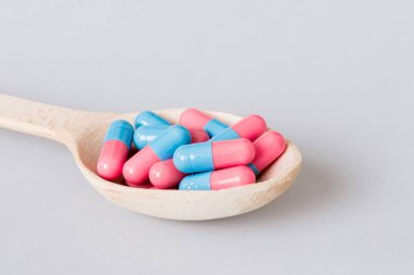 Vitamin capsules in a spoon on a colored background. Pills served as a healthy meal. Red soft gel vitamin supplement capsules on spoon.