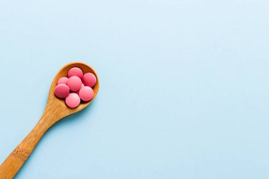 Vitamin capsules in a spoon on a colored background. Pills served as a healthy meal. Red soft gel vitamin supplement capsules on spoon.