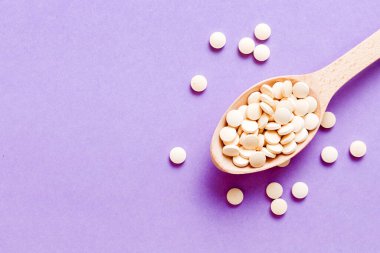 Renkli arka planda bir yığın beyaz hap. Tabletler masaya saçılmış. Kırmızı yumuşak jelatin kapsül yığını. Vitaminler ve beslenme takviyeleri konsepti.