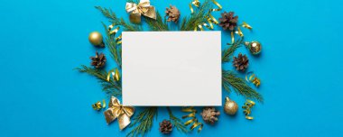 Noel kompozisyonu düzdü. Kare kağıt boş, çam ağacı dalları, renkli arka planda noel süslemeleri. Üst görünüm, metin için boşluk kopyala.