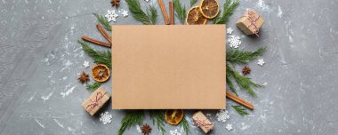 Noel kompozisyonu düzdü. Kare kağıt boş, çam ağacı dalları, renkli arka planda noel süslemeleri. Üst görünüm, metin için boşluk kopyala.