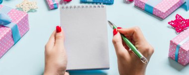 Kadın elinin mavi arka planda notlar alırken üst görüntüsü. Yeni yıl süslemeleri ve oyuncakları. Noel zamanı konsepti.