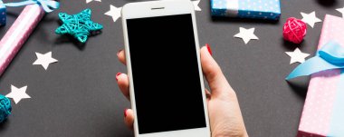 Bayramlık siyah arka planda kadın elinin telefonunun üst görüntüsü. Noel süsleri. Yeni yıl tatili. Model.