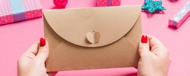 Bayram süslemelerinden yapılmış pembe arka planda bir zarf tutan kadının üst görüntüsü. Noel zamanı konsepti.