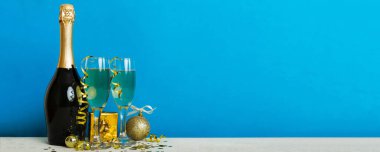 Champagne bottle with confetti, glasses and christmas decor on colored holiday background. Flat lay New Year decorations.