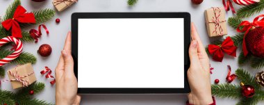 Evden Noel alışverişi, kadın elleri boş beyaz ekranlı tableti tutuyor. Kadın elinde tablet, boş ekran, Noel ağacı ve arka planda hediyeler..