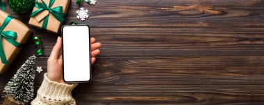 Mesaj atmak için yeri olan bir Noel modeli. Noel reklamı, uygulama şablonu. Masa arkasında boş ekran olan el ele tutuşan telefon. Mutlu yıllar ve Xmas Flat.