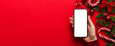 Mesaj atmak için yeri olan bir Noel modeli. Noel reklamı, uygulama şablonu. Masa arkasında boş ekran olan el ele tutuşan telefon. Mutlu yıllar ve Xmas Flat.