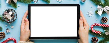 Evden Noel alışverişi, kadın elleri boş beyaz ekranlı tableti tutuyor. Kadın elinde tablet, boş ekran, Noel ağacı ve arka planda hediyeler..