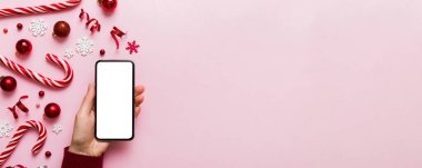 Mesaj atmak için yeri olan bir Noel modeli. Noel reklamı, uygulama şablonu. Masa arkasında boş ekran olan el ele tutuşan telefon. Mutlu yıllar ve Xmas Flat.