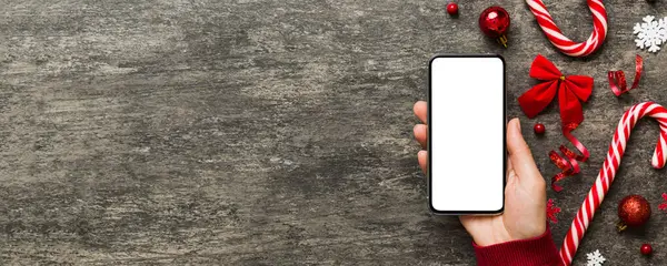 Mesaj atmak için yeri olan bir Noel modeli. Noel reklamı, uygulama şablonu. Masa arkasında boş ekran olan el ele tutuşan telefon. Mutlu yıllar ve Xmas Flat.