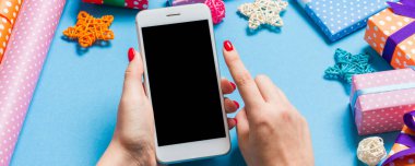 Neşeli mavi arka planda kadın elinin telefonunun üst görüntüsü. Noel süsleri. Yeni yıl tatili. Model.