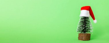 One small Christmas tree with santa hat on colored background. new year decoration with copy space.