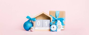 1 january. Christmas composition on colored background with a wooden calendar, with a gift box, toys, bauble copy space.