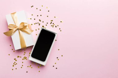 Altın kurdeleli hediye kutusu ve arka planda akıllı telefon, üst manzara. Boş kutu paketleme modeli, tasarımınız için şablon - markalaşma modeli.