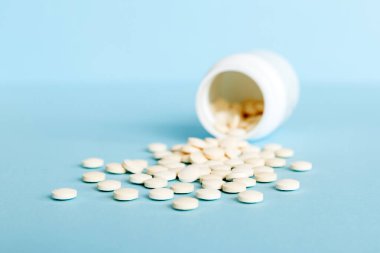 İlaç şişesi ve beyaz haplar arka plana dökülmüş. İlaçlar ve reçeteli haplar arka plandaydı. İlaç şişesinden beyaz ilaç ve haplar dökülüyor..