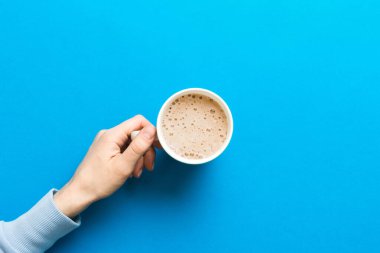 Renkli arka planda bir fincan kahve tutan minimalist stil bir kadın. Düz yerde, kapuçino bardağının üstünde. Metin için boş yer, kopyalama alanı. Kahve bağımlılığı. Üst manzara, düz uzanma.