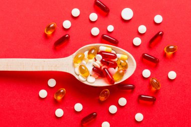 Renkli bir arka planda kaşıkta vitamin kapsülleri. Haplar sağlıklı bir yemek olarak sunuldu. Kırmızı yumuşak jel vitamin takviye kapsülleri kaşık üzerinde.