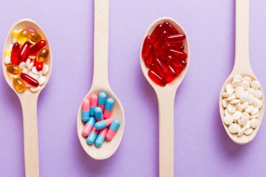 Vitamin capsules in a spoon on a colored background. Pills served as a healthy meal. Red soft gel vitamin supplement capsules on spoon.