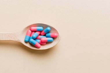 Renkli bir arka planda kaşıkta vitamin kapsülleri. Haplar sağlıklı bir yemek olarak sunuldu. Kırmızı yumuşak jel vitamin takviye kapsülleri kaşık üzerinde.