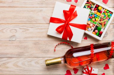 Sevgililer Günü için renkli arka planda bir şişe kırmızı şarap hediye ve çikolatalı. Kalp, hediye kutusuyla şekillendirilmiş çikolatalar fotokopi alanı ile üst görünüm.