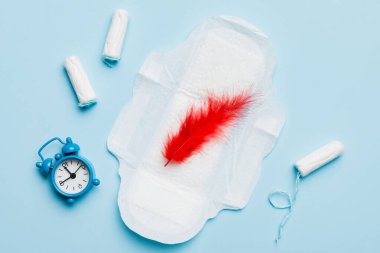 Alarm saatini hijyenik kadın tamponları ve regl pedleri ile çalıyor. Tıbbi konsept kadın kritik günler ve regl dönemi. Kadın günlük hijyen. Boşluğu kopyala.