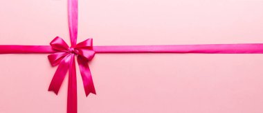 Mor kurdelenin üst görüntüsü yuvarlandı ve pembe fiyonk renkli arka planda izole edildi. Kopyalama alanı olan düz.