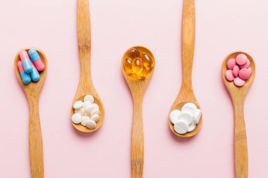 Renkli bir arka planda kaşıkta vitamin kapsülleri. Haplar sağlıklı bir yemek olarak sunuldu. Kırmızı yumuşak jel vitamin takviye kapsülleri kaşık üzerinde.