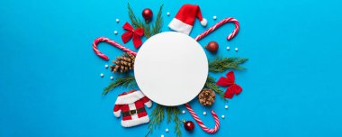 Noel kompozisyonu düzdü. Yuvarlak kağıt boş, çam ağacı dalları, renkli arka planda noel süslemeleri. Üst görünüm, metin için boşluk kopyala.