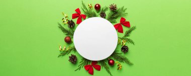 Noel kompozisyonu düzdü. Yuvarlak kağıt boş, çam ağacı dalları, renkli arka planda noel süslemeleri. Üst görünüm, metin için boşluk kopyala.
