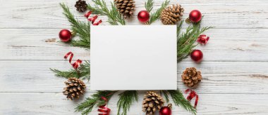 Noel kompozisyonu düzdü. Kare kağıt boş, çam ağacı dalları, renkli arka planda noel süslemeleri. Üst görünüm, metin için boşluk kopyala.