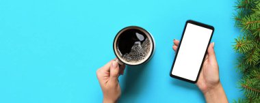 Boş beyaz ekran ve kahve bir fincan siyah cep telefonu tutan eller. Mockup görüntü kopya alanı ile. Üstten görünüm mavi arka plan, düz üzerinde yatıyordu.