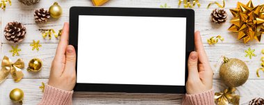 Evden Noel alışverişi, kadın elleri boş beyaz ekranlı tableti tutuyor. Kadın elinde tablet, boş ekran, Noel ağacı ve arka planda hediyeler..