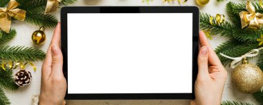 Evden Noel alışverişi, kadın elleri boş beyaz ekranlı tableti tutuyor. Kadın elinde tablet, boş ekran, Noel ağacı ve arka planda hediyeler..
