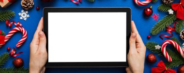 Evden Noel alışverişi, kadın elleri boş beyaz ekranlı tableti tutuyor. Kadın elinde tablet, boş ekran, Noel ağacı ve arka planda hediyeler..