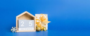 25 december. Christmas composition on colored background with a wooden calendar, with a gift box, toys, bauble copy space.