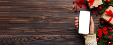 Mesaj atmak için yeri olan bir Noel modeli. Noel reklamı, uygulama şablonu. Masa arkasında boş ekran olan el ele tutuşan telefon. Mutlu yıllar ve Xmas Flat.