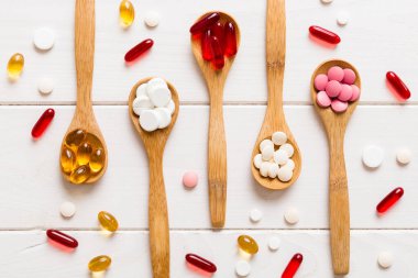 Renkli bir arka planda kaşıkta vitamin kapsülleri. Haplar sağlıklı bir yemek olarak sunuldu. Kırmızı yumuşak jel vitamin takviye kapsülleri kaşık üzerinde.