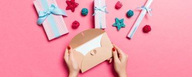 Bayram süslemelerinden yapılmış pembe arka planda bir zarf tutan kadının üst görüntüsü. Noel zamanı konsepti.