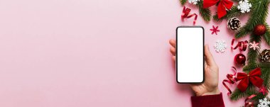 Mesaj atmak için yeri olan bir Noel modeli. Noel reklamı, uygulama şablonu. Masa arkasında boş ekran olan el ele tutuşan telefon. Mutlu yıllar ve Xmas Flat.