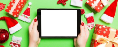 Elinde tabletle Noel süslemelerinden yapılmış yeşil arka planda gezen kadının üst görüntüsü. Yeni yıl tatili konsepti. Model.