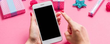 Neşeli pembe arka planda kadın elinin telefonunun üst görüntüsü. Noel süsleri. Yeni yıl tatili. Model.