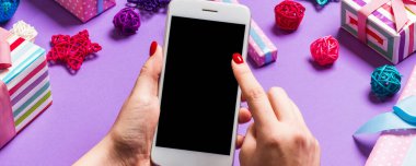 Bayramlık mor arka planda kadın elinin telefonunun üst görüntüsü. Noel süsleri. Yeni yıl tatili. Model.