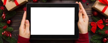 Evden Noel alışverişi, kadın elleri boş beyaz ekranlı tableti tutuyor. Kadın elinde tablet, boş ekran, Noel ağacı ve arka planda hediyeler..