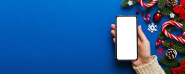 Mesaj atmak için yeri olan bir Noel modeli. Noel reklamı, uygulama şablonu. Masa arkasında boş ekran olan el ele tutuşan telefon. Mutlu yıllar ve Xmas Flat.