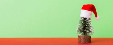One small Christmas tree with santa hat on colored background. new year decoration with copy space.