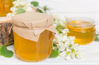 Tatlı bal kavanozu bahar akasyası çiçeklerini sarmıştı. Kavanozdaki kaşıktan bal akar. Tahta zemin üzerinde taze akasya balı kavanozları.