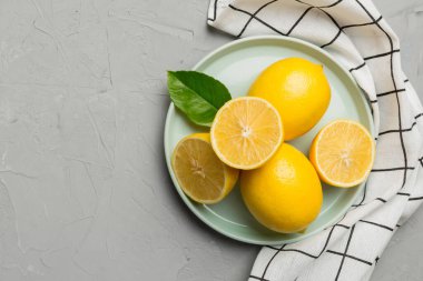 Taze kesilmiş limon ve tüm limonları renkli arka planda yuvarlak tabakta. Yemek ve içecek malzemeleri hazırlanıyor. Sağlıklı beslenme teması üst görünüm kopyalama alanı.