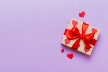 Top view photo of valentine day decorations gift box with red ribbon bow on colored background. Holiday gift boxes with top view.