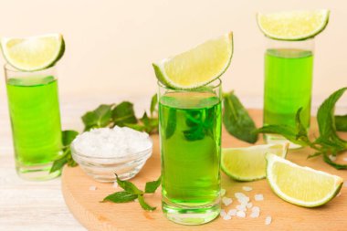 Tatlı ferahlatıcı nane likörü, masa arkasında buz ve nane yaprakları, limon dilimi ve nane aromalı shot.